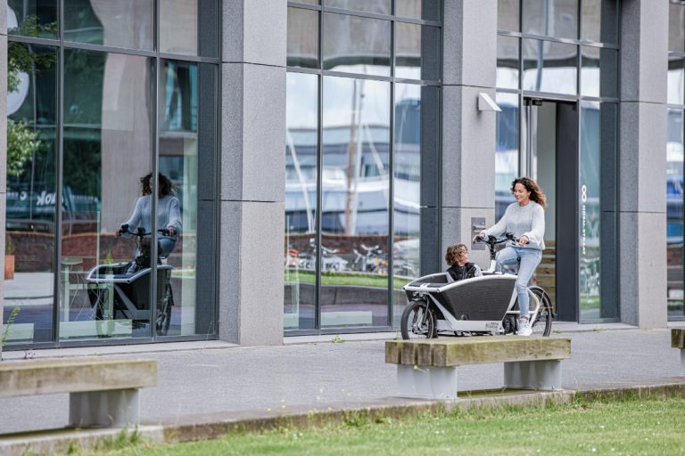 Afgebeeld is een witte vrouw die op een bakfiets fietst. In de bakfiets zit een kind. ASML Op 27 september 2021 openen wethouder Steven Kraaijeveld en Teun Wartenbergh van ASML in Eersel de ‘Park&Ride Duynenwater’ met de grootste e-bike hub van Nederland. Het is ook de eerste mobiliteitshub voor ASML waarmee werknemers na het parkeren van hun auto, per fiets naar kantoorlocaties in en rond Veldhoven kunnen gaan. Voor deze P&R met 300 e-bikes werkt ASML samen met mobiliteitsaanbieder Hely.
