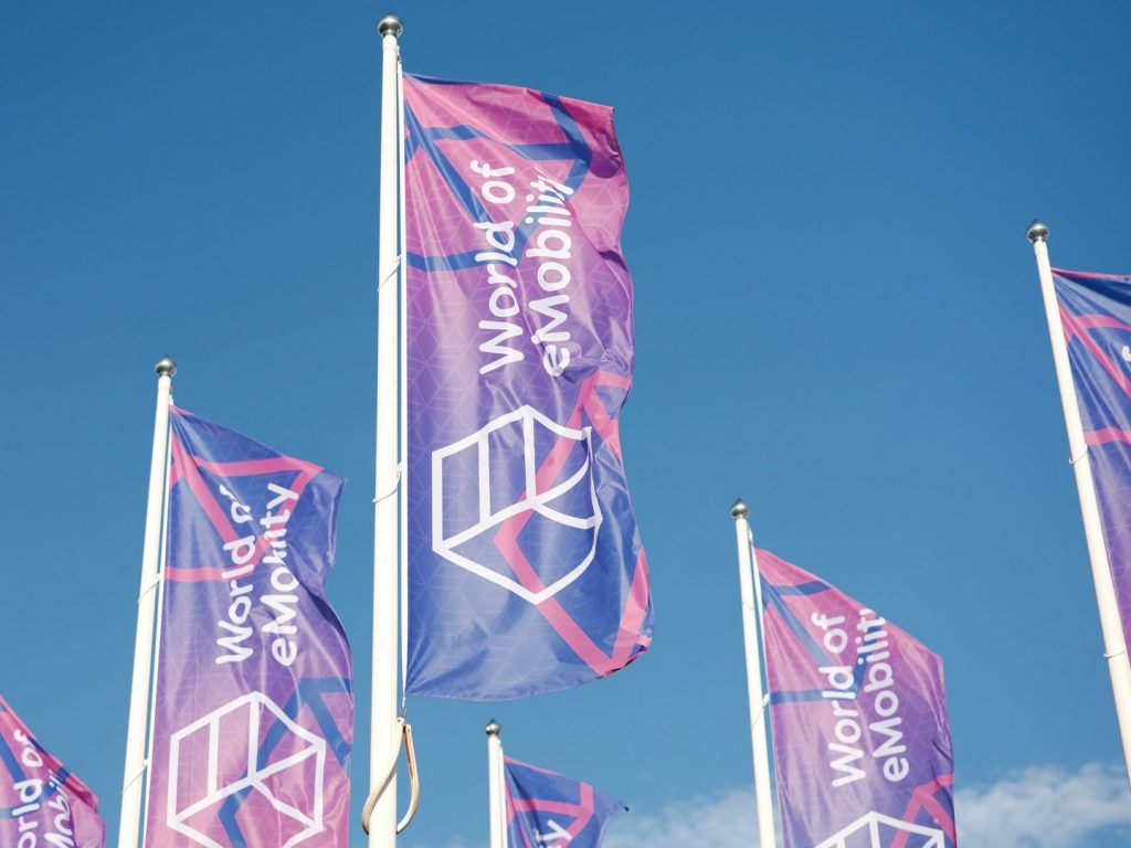 2022 03 08 world of emobility uitgelicht | Op 27, 28 en 29 oktober 2022 kunnen particuliere en zakelijke bezoekers uit de eMobility-industrie hun hart ophalen tijdens de tweede editie van World of eMobility. Afgebeeld staan vier vlaggen met daarop het logo van World of eMobility.
