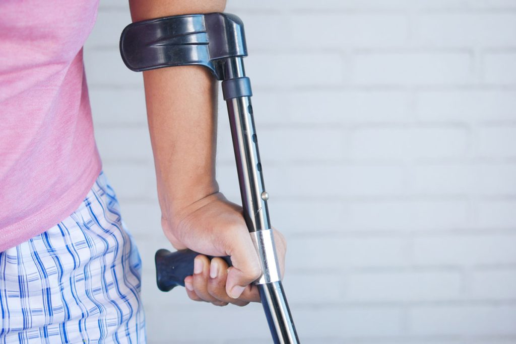 HeadFirst Group en Alicia introduceren één-klik-arbeidsongeschiktheidsvoorziening voor zzp’ers arbeidsongeschiktheidsvoorziening zzp’ers. Afgebeeld staat een witte rechterhand die leunt op een kruk. De persoon draagt verder een lichtroze T-shirt en een witte broek met blauwe ruiten.